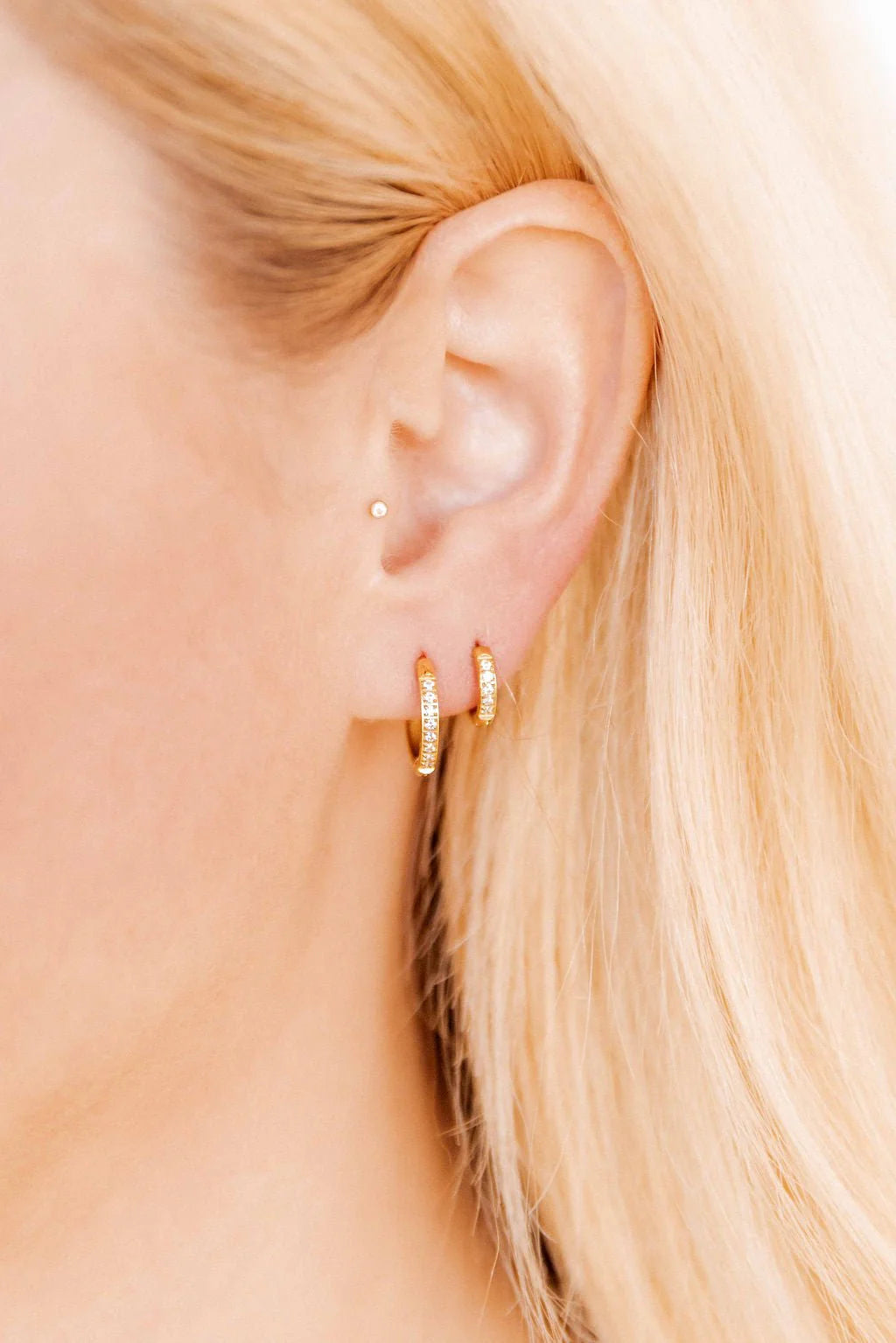 Close-up of an ear wearing gold hoop earrings with blonde hair.